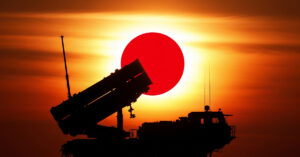 A ground-based missile launcher silhouetted against a rising sun, with a Japanese flag subtly integrated into the background, symbolizing the military deployment and strategic partnership between the two nations.