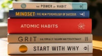 A stack of five inspirational books, including "Atomic Habits" and "Mindset," illuminated by sunlight on a wooden desk.