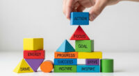 A person's hand stacking colorful, geometric blocks with various inspiring words like "Focus," "Action," "Goal," and "Energy" written on them, illustrating the concept of building motivation.